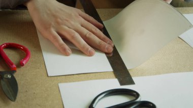 Tecrübeli bir zanaatkarın elleri cetvel boyunca düz bir kağıt katlar. El yapımı ayakkabılar için desenler oluşturuluyor.