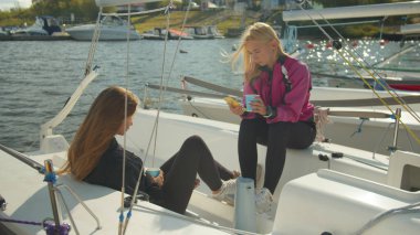 Sarışın ve esmer denizciler sonbaharda bir yatta dinlenirler. Kahve içip internette akıllı telefonlarıyla sörf yapıyorlar..