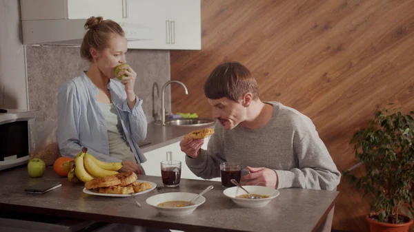 Una escena de la vida familiar de una pareja joven. Desayuno juntos en el nuevo apartamento en la cocina.La mujer muerde una manzana. Movimiento lento. — Foto de Stock