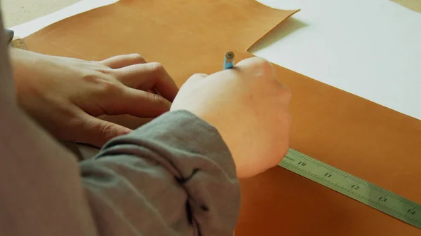 Slow-motion video van een kleermaker handen maken van een close-up markering en snijlijn met een potlood en liniaal op een stuk natuurlijk bruin leer. — Stockfoto