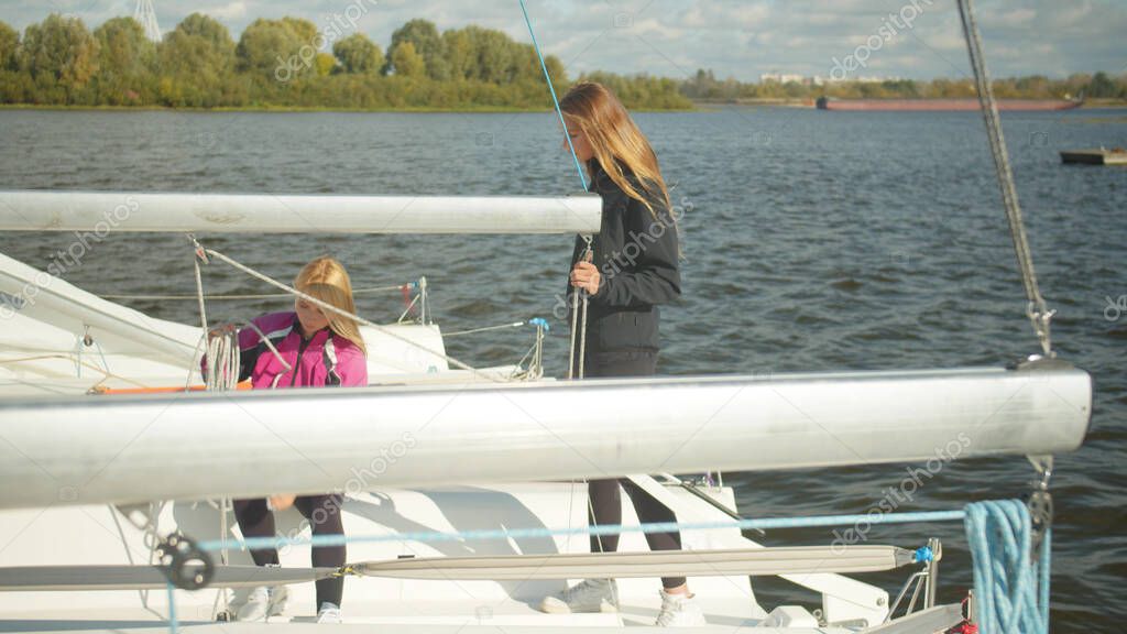 End of the sailing season. On a cold autumn day, female sailing athletes dismantle the rigging of the yacht for winter in the dock.