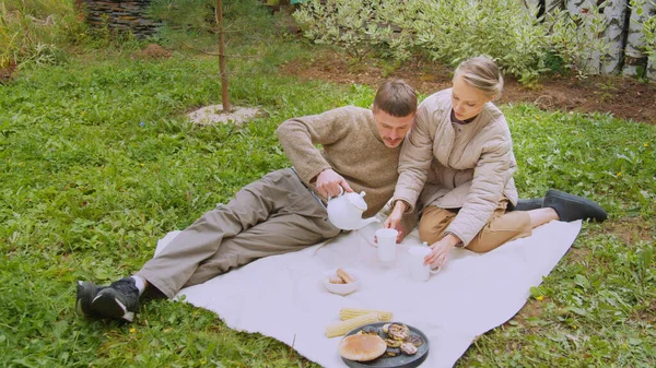 Парень и девушка пьют чай из чайника, сидя на лужайке в природе. В сельском саду. — стоковое фото