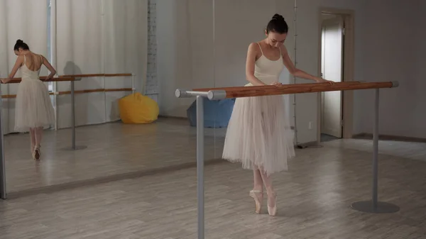 Une belle ballerine se tient debout sur le rail de ballet et étire ses jambes devant le miroir — Photo