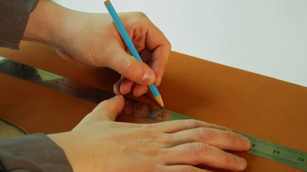 Ο τσαγκάρης φτιάχνει ένα σχέδιο για μπότες από γνήσιο δέρμα. Χρησιμοποιήστε ένα μολύβι και χάρακα για να σχεδιάσετε μια ευθεία γραμμή για το κόψιμο. — Φωτογραφία Αρχείου