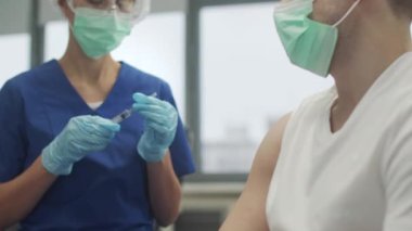 Bir klinikte koronavirüse karşı aşı olan bir adamın yakın plan çekiminde, bir doktor şırınga yapar, yavaş çekimde..
