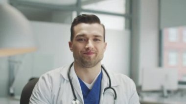 Olumlu gülümseyen genç bir doktor doğrudan kameraya bakar. Otelin tıbbi ofisinde yakın plan bir portre..