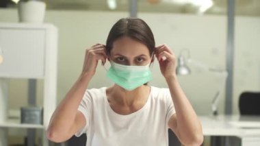 Şirin bir kadın yüzüne ofis raflarının arkasına tıbbi maske takıyor.