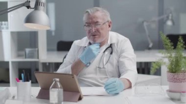 Doktorun iş arkadaşlarıyla internet üzerinden tabletle yaptığı bir video konferansı. Yetişkin bir doktor hastanedeki ofisinden çevrimiçi olarak güvenilir doktorlara danışır.