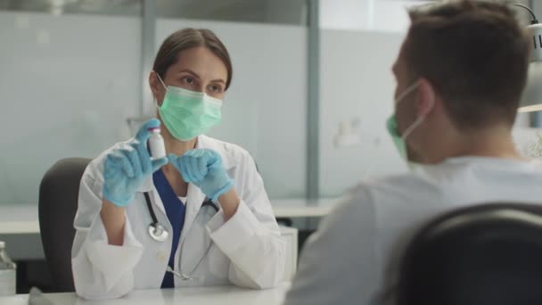 Egy fiatal orvosnő egy üveg oltóanyagot tart a kezében, és bemutatja. — Stock videók