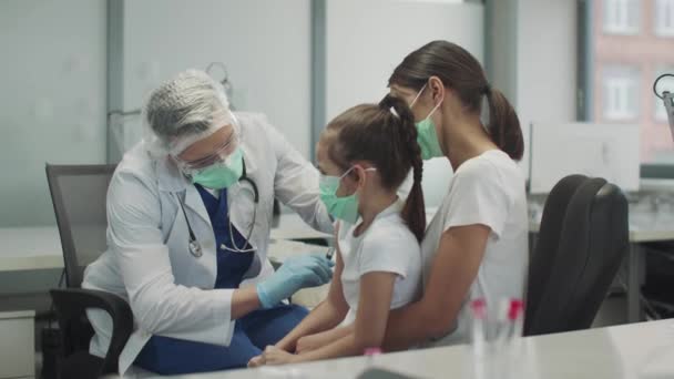 A kind doctor in protective glasses and a mask has given the child a girl a shot in the arm and nods approvingly to her, slowmotion. — Stock Video