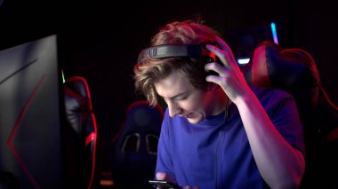 Genç bir adam çevrimiçi video oyunu sırasında telefon alıyor, kulaklıklarını çıkarıyor ve konuşmaya gidiyor.