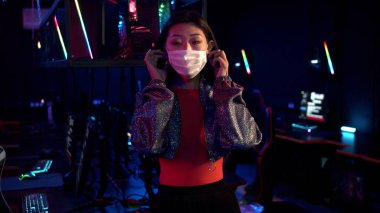 Bilgisayar kulübündeki tatlı Asyalı kız tıbbi maskesini çıkarıp kameraya gülümsüyor.