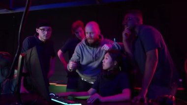 Atıcılık şampiyonasından önceki antrenman sırasında koç takıma stratejilerini açıklar, kız bilgisayarda oynar.