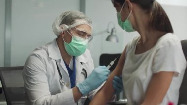 Tıbbi maskeli ve koruyucu gözlüklü genç bir doktor hastaların kollarına koronavirüs için antiviral ilaç enjekte eder..