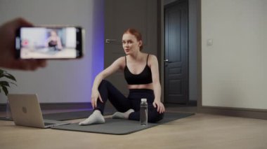 Kadın yoga eğitmeni video dersi veriyor, su içiyor ve meditasyon yapıyor.