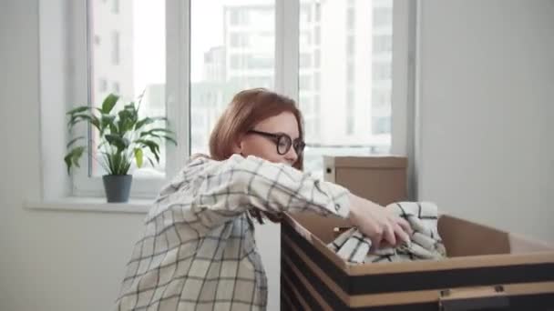 戴眼镜的妇女从纸板箱中取出毛毯 — 图库视频影像