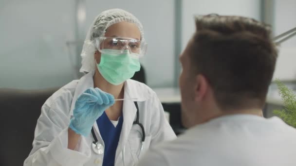 Молодая женщина-врач в клинике берет мазок у пациентов носоглотки для анализа на ковид-19 — стоковое видео