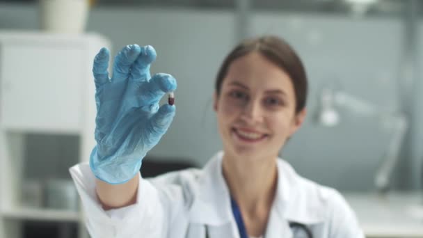 Médico feminino bonito segura uma cápsula de medicamento na mão, close-up da mão — Vídeo de Stock