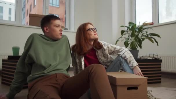 Paar sitzt auf Parkettboden und begutachtet Wände einer neuen Wohnung — Stockvideo