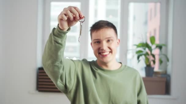 Egy fiatal fickó áll egy fehér üres szobában, és mosollyal rázza a kulcsokat. — Stock videók