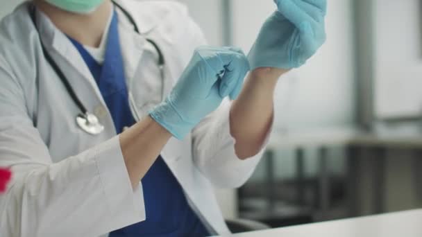 Medicul din cabinetul medical se pregătește să primească pacienți și să efectueze vaccinarea împotriva covid-19. El pune pe mănuși de protecție din cauciuc albastru . — Videoclip de stoc