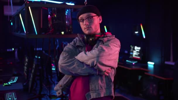 An experienced gamer in a hat and glasses poses for a video presentation of the team at the online games championship, with his arms folded — Stock Video