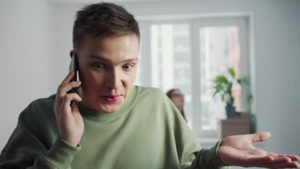 A fiatalember élénken beszél a telefonban. A háttérben egy lány kóborol a szobában. — Stock videók