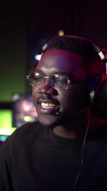 Gözlüklü ve kulaklıklı Afro-Amerikalı bir adam bilgisayarda oynuyor ve konuşuyor, takıma ipuçları veriyor, gülümsüyor.