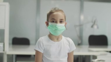 Ofis masalarının arka planında bir bebek maske takıp kameraya bakıyor.