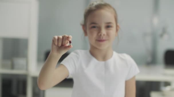 Gadis kecil yang lucu tersenyum dan memegang kapsul obat di tangannya dekat, lamban. — Stok Video