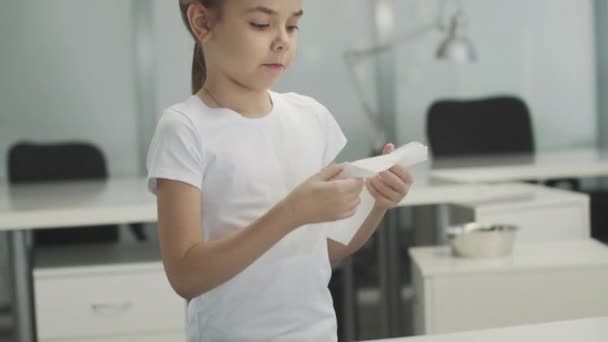 En söt liten flicka barn plockar upp en vit servett från bordet och blåser näsan i den — Stockvideo