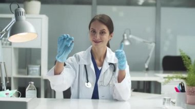 Genç bir esmer kız elinde bir ilaç kapsülü tutuyor ve ona benzer bir şeyi diğer eliyle gösteriyor.