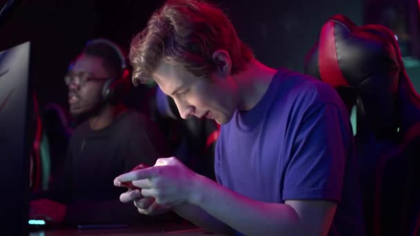 Милий молодий чоловік в комп'ютерному клубі вирішив зняти свою думку з комп'ютера, виграв гру на смартфоні і щасливий — стокове відео