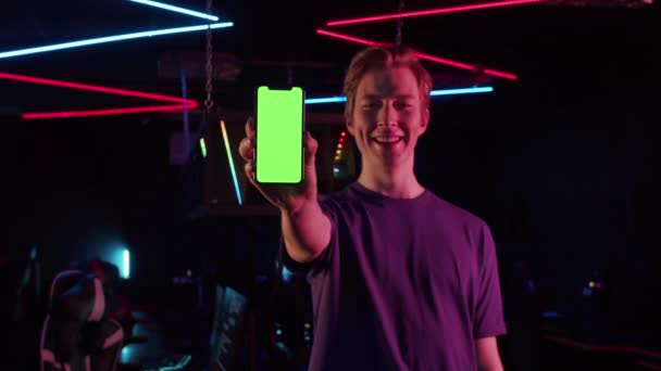 Een leuke gamer in een T-shirt houdt een nieuw model van een gaming smartphone in zijn hand en toont het aan de camera van dichtbij — Stockvideo