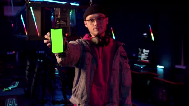 Молодий геймер у джинсовій куртці тримає новий смартфон у камері і показує його крупним планом — стокове відео