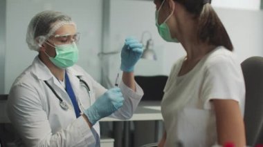 Deneyimli bir pratisyen doktor genç bir hastayı koronavirüse karşı aşılamaya hazırlanıyor. Aşı şırıngasına parmağını şaklatıyor..