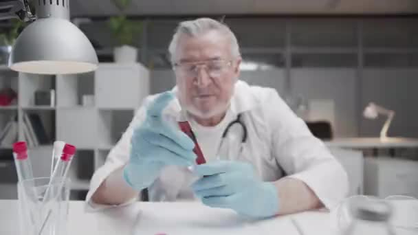 Опытный лаборант с седыми волосами исследует образец крови пациента в стеклянной трубке. Ветеринарная больница. — стоковое видео