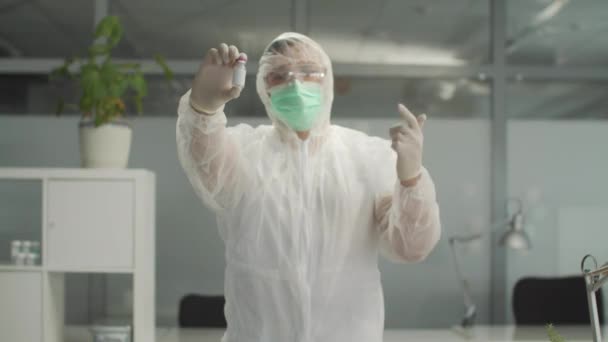 Na klinice ukazuje lékař v ochranném obleku lahvičku vakcíny a doporučuje ji — Stock video