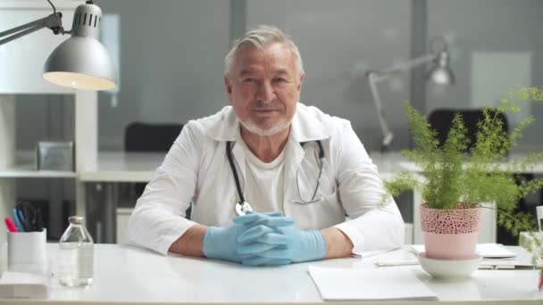 Хороший доктор со стетоскопом вокруг шеи улыбается в своем кабинете — стоковое видео