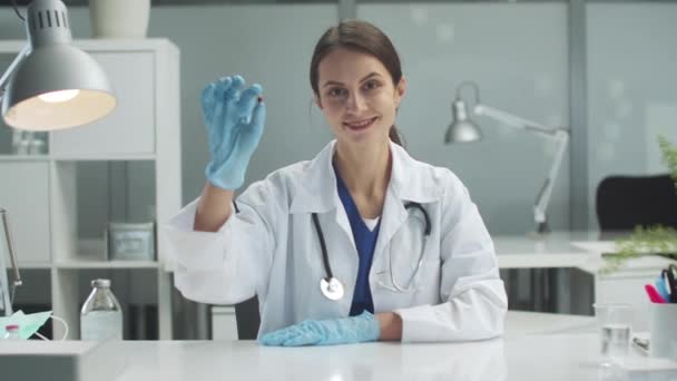 Una giovane dottoressa tiene in mano una capsula medicinale e la esamina al tavolo della clinica, rallentando. — Video Stock