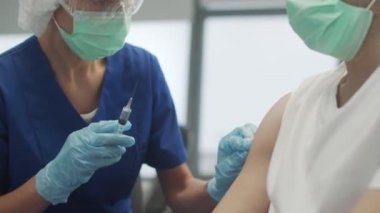 Klinikte koronavirüse karşı aşı olan bir adamın yakın plan çekiminde, bir doktor şırınga enjekte eder.