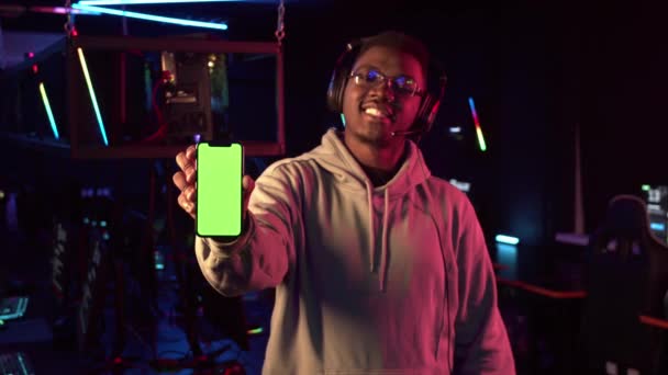 Närbild av den nya smartphone, i bakgrunden är det hålls i händerna på en erfaren svart spelare med hörlurar — Stockvideo