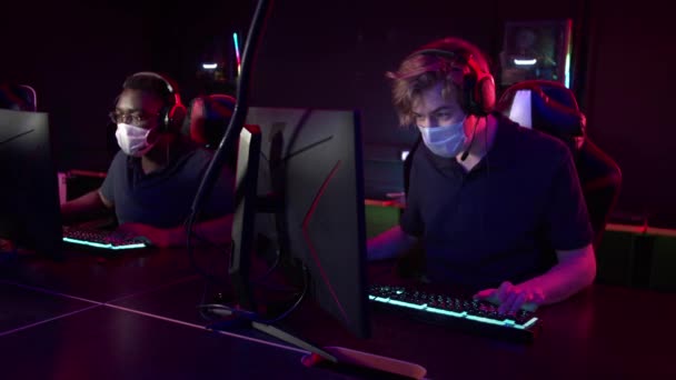 Jóvenes con máscaras médicas juegan en un club de informática durante la pandemia de covid-19 — Vídeo de stock