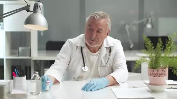 Взрослый врач счастлив получить коронавирусную вакцину, показывает бутылку в руках — стоковое видео