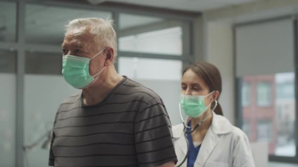Um paciente idoso tem sintomas de coronavírus, tosse, uma médica escuta seus pulmões — Vídeo de Stock