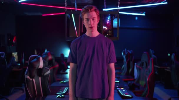 A young gamer guy poses against the background of a well-equipped computer room in neon light — Stock Video