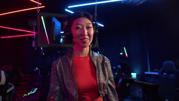 Mignonne asiatique fille dans un club informatique met sur un casque et appelle avec son doigt pour la rejoindre — Video