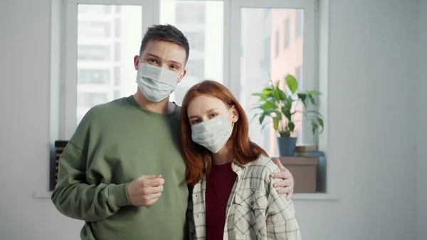 Couple in medical masks stands in an empty apartment and shows the key to the camera