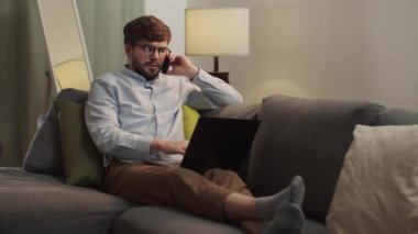 Avrupalı bir adam telefonla konuşuyor ve bir dizüstü bilgisayar üzerinde çalışıyor..