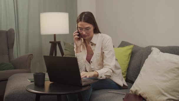 Спокойная европейская женщина работает дома за компьютером и разговаривает по телефону. — стоковое видео